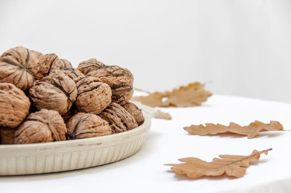 Free Image of Walnuts in a ceramic bowl with dry leaves on white table 