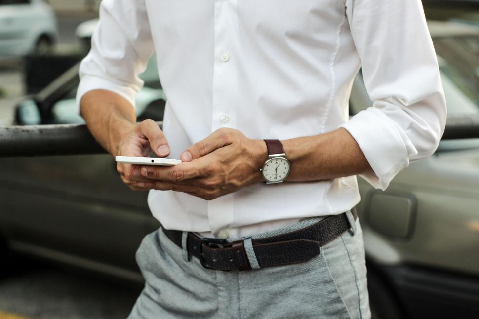 Free Image of Man checking his smartphone against a car background. 