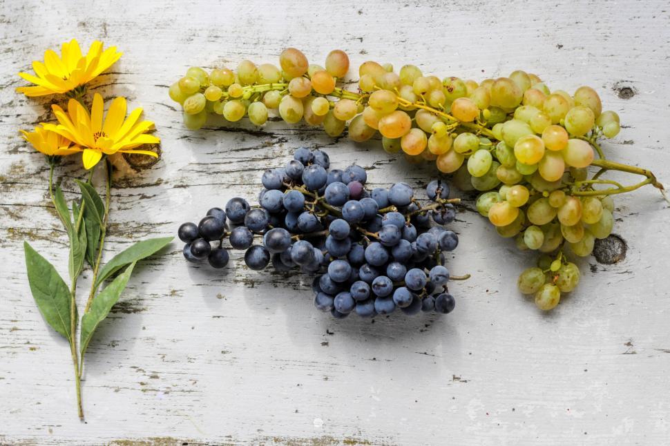 Free Image of Yellow flowers and grapes composition on wooden surface 