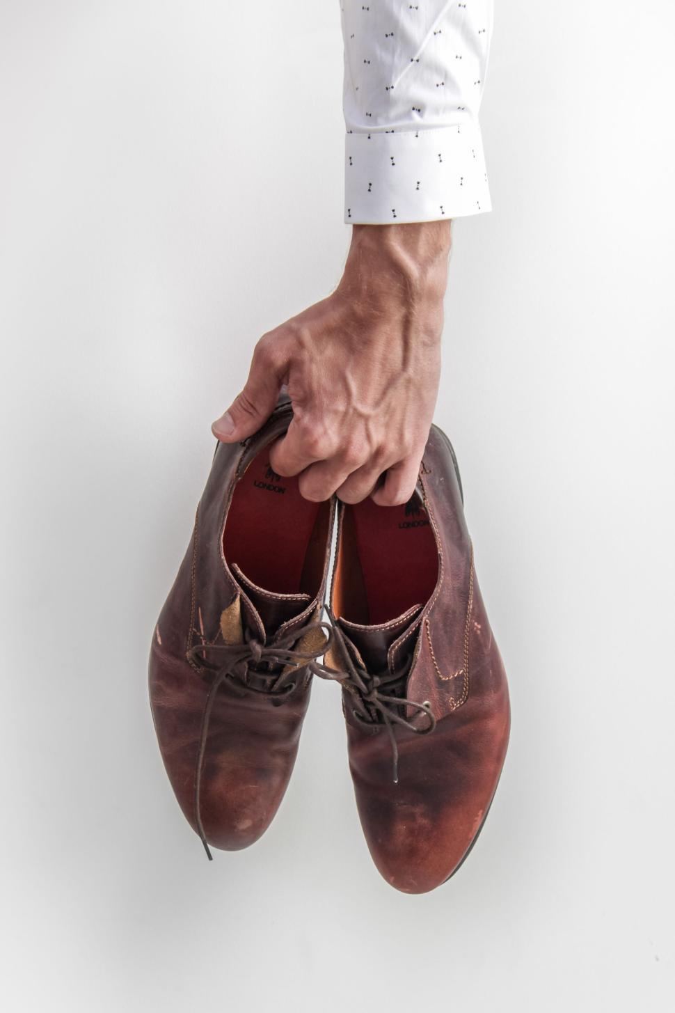 Free Image of Hand holding polished brown leather shoes with laces. 