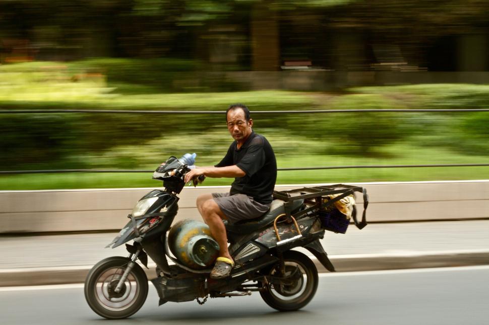Free Image of Man riding a motor scooter down the city street swiftly 