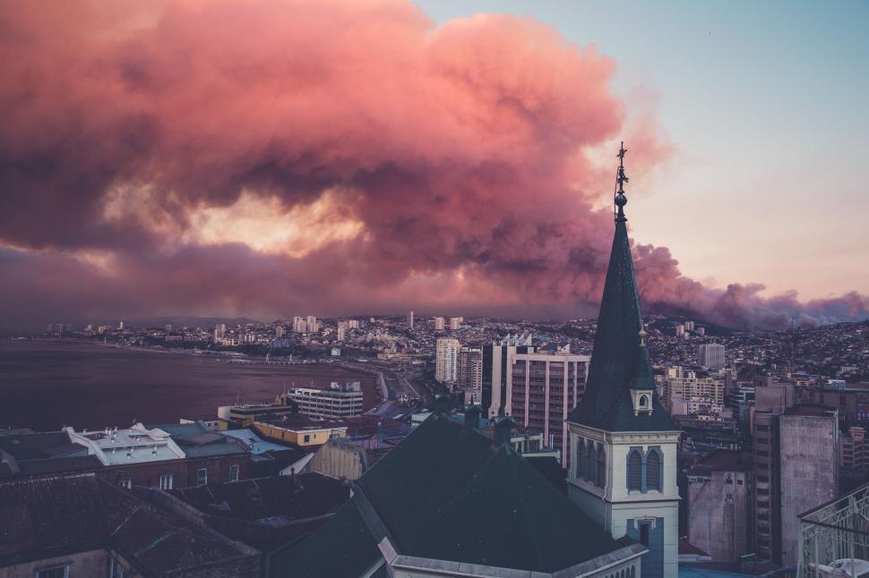 Free Image of View of a city at sunset with dramatic clouds and smoke. 