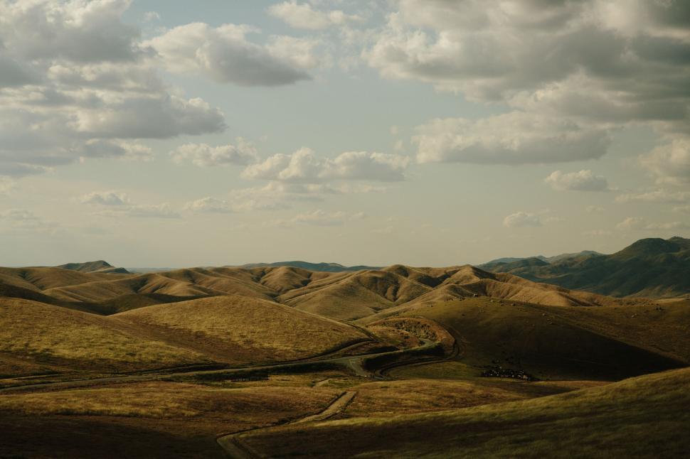 Free Image of Rolling hills under a cloudy sky at sunset time 