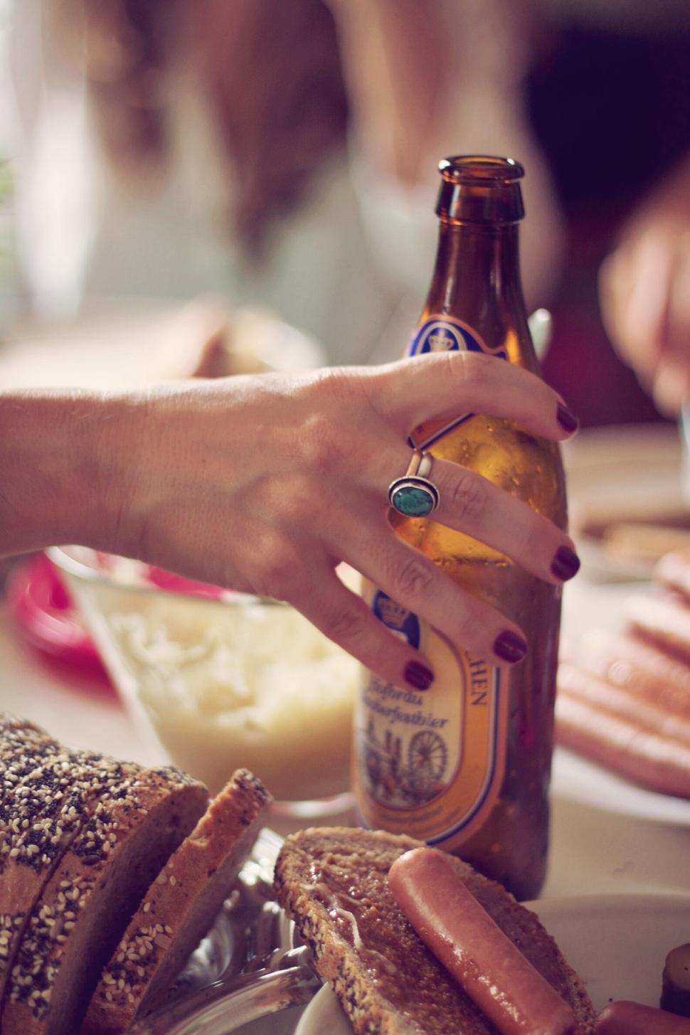 Free Image of Hand holding beer bottle near food on a table 