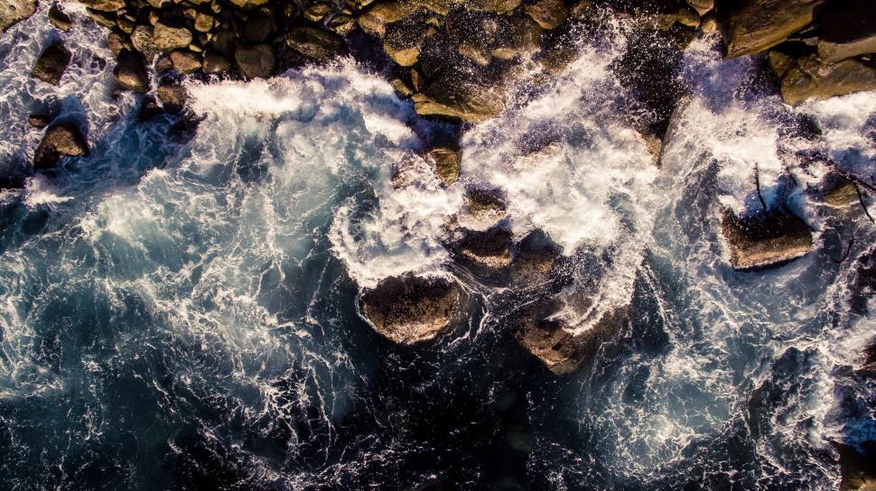 Free Image of Overhead view of waves crashing on rocky shoreline. 