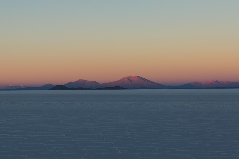 Free Image of Sunset over expansive salt flats with distant mountains 