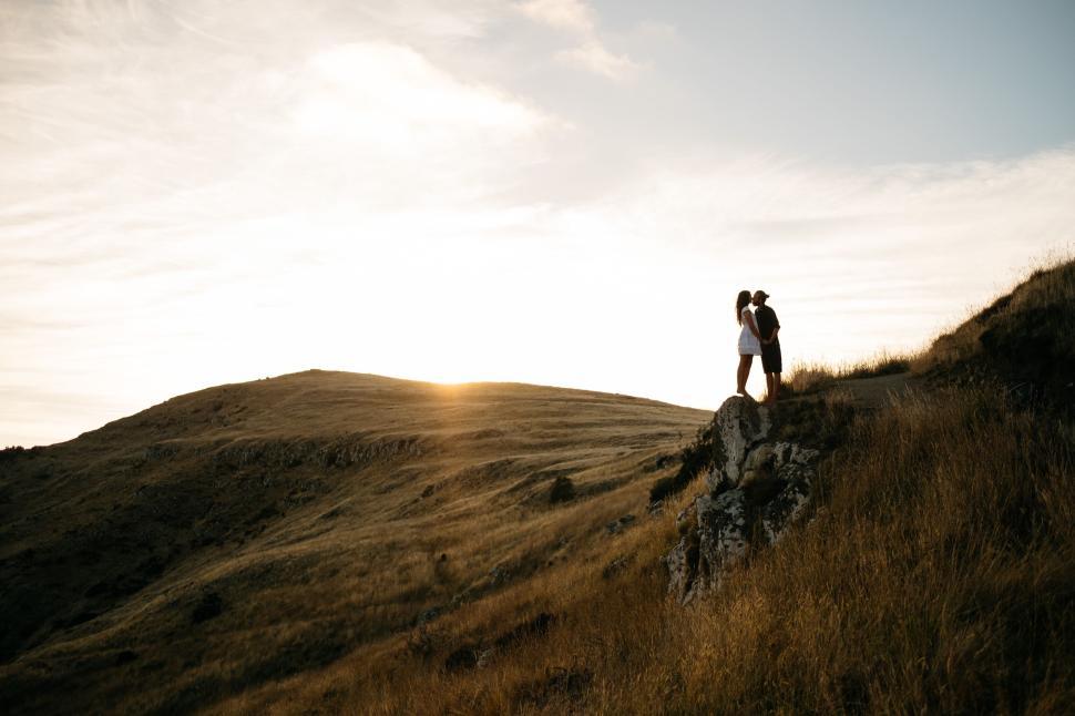 Free Image of Couple stands on hilltop at sunset embracing each other. 