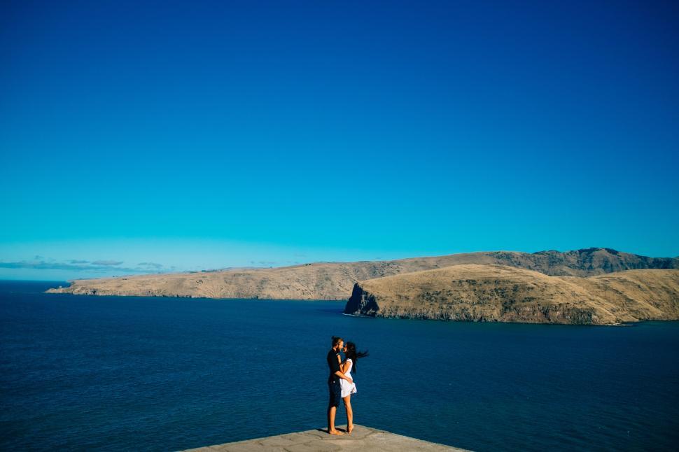 Free Image of Couple shares moment by the ocean under clear sky. 