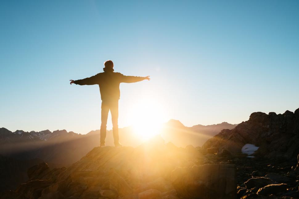 Free Image of Person stands on mountaintop with arms wide in sunset. 
