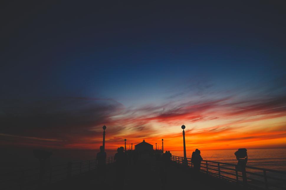 Free Image of Sunset pier with silhouetted figures watching skyline 