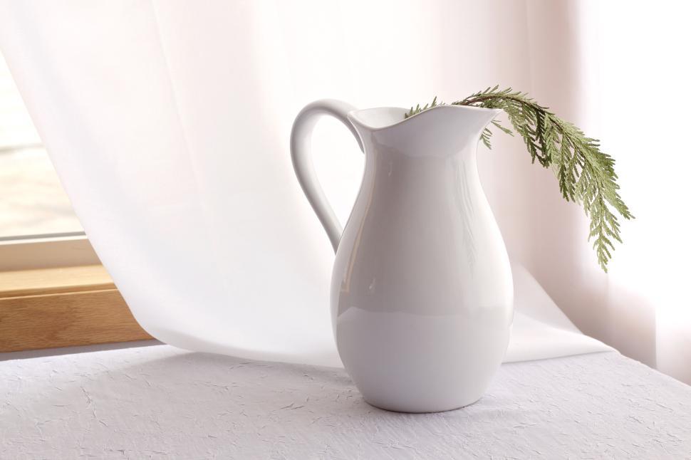 Free Image of White ceramic jug with green branch on table, natural aesthetic. 