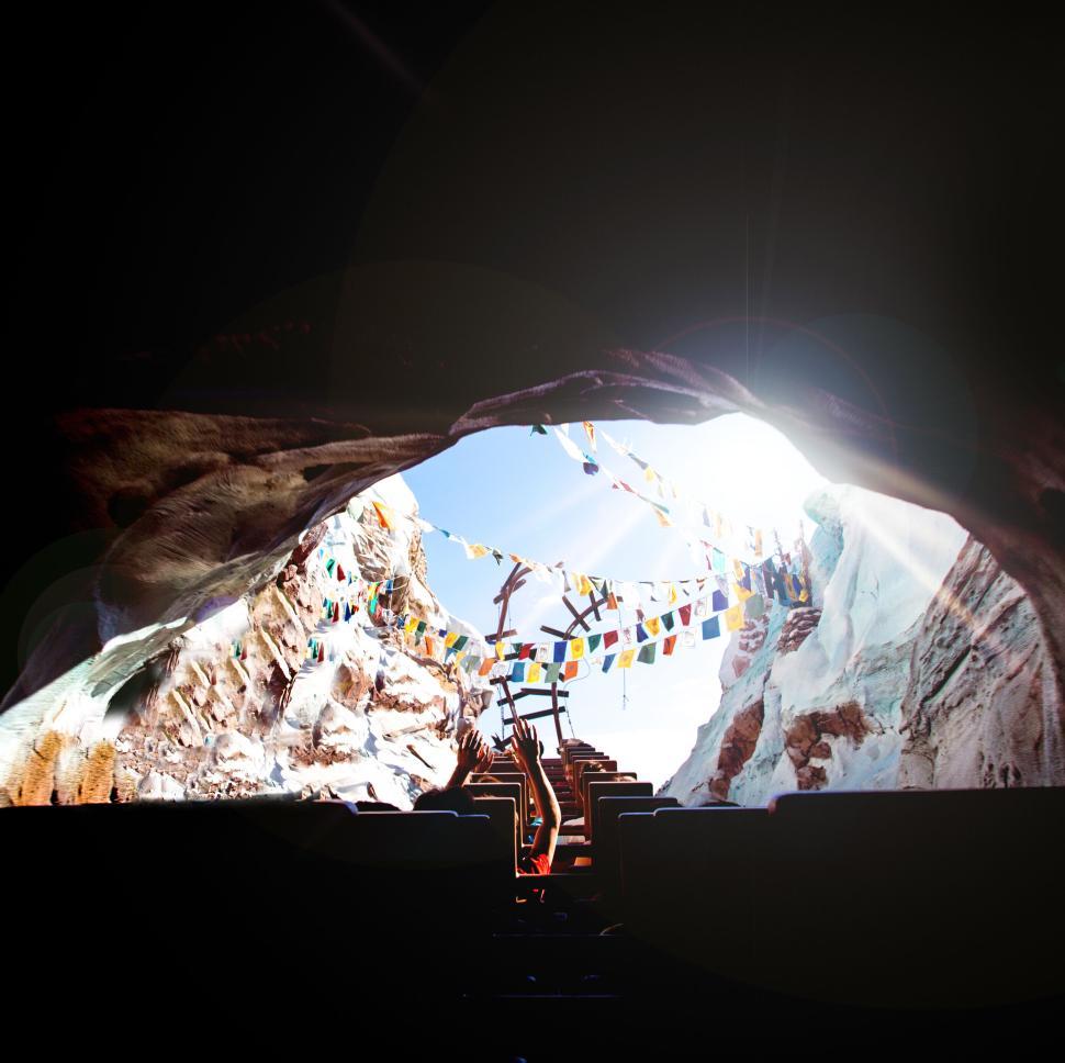Free Image of Roller coaster entering a dark cave with flags. 