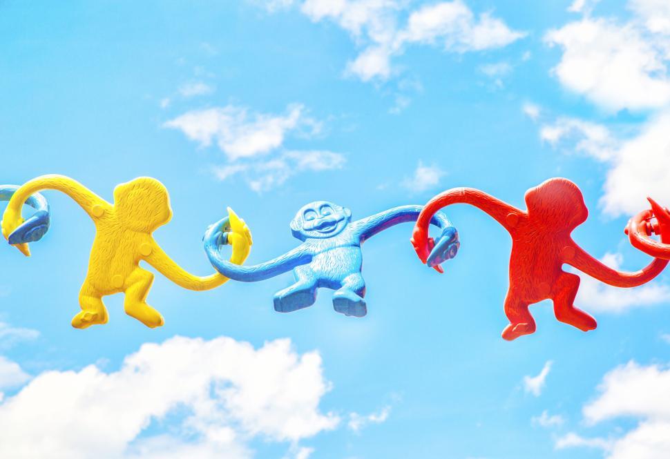 Free Image of Colorful plastic monkeys holding hands under a sky. 