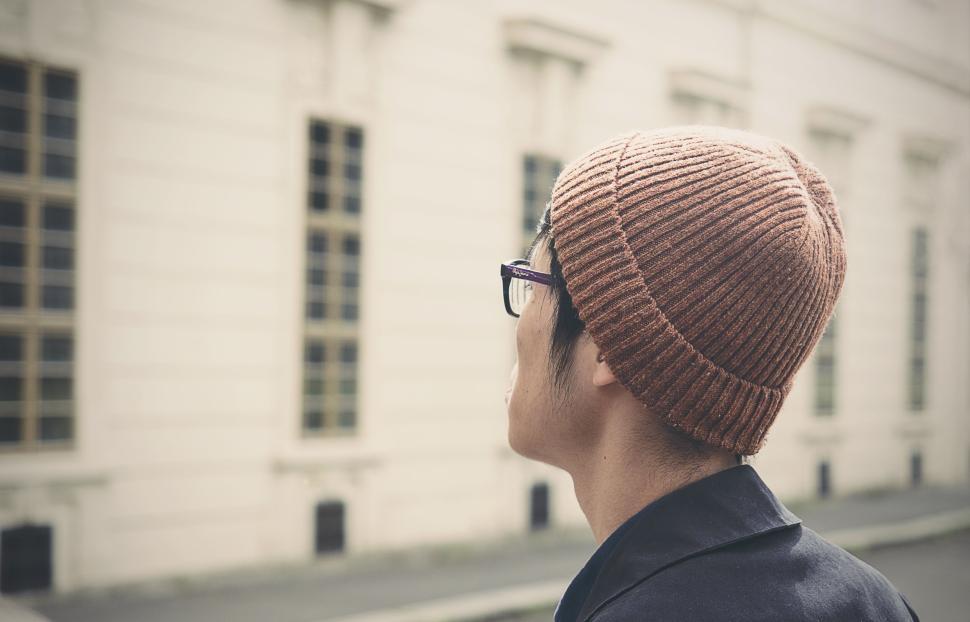 Free Image of Person wears brown beanie looks up at picturesque building. 
