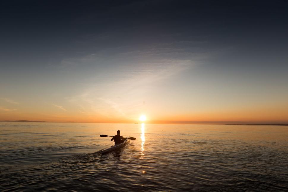 Free Image of Kayaker paddling towards sunset on calm ocean waters. 