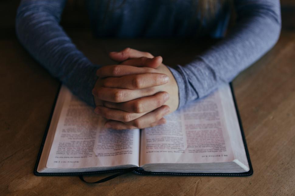 Free Image of Person praying with hands over an open book, indoors. 