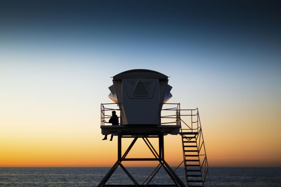 Free Image of Silhouetted person in lifeguard tower at sunset. 