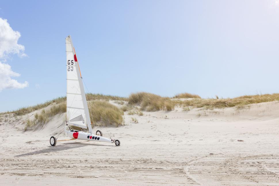 Free Image of White sand beach with a sleek sailboat sky backdrop 