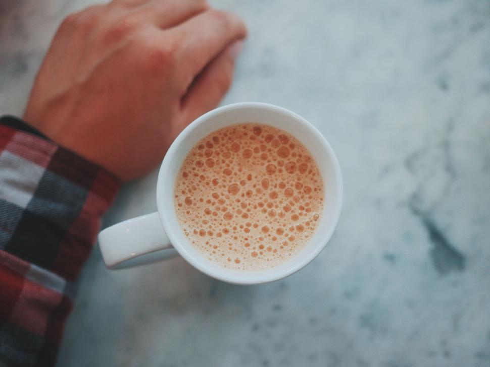 Free Image of Hand rests near frothy coffee cup on marble surface 