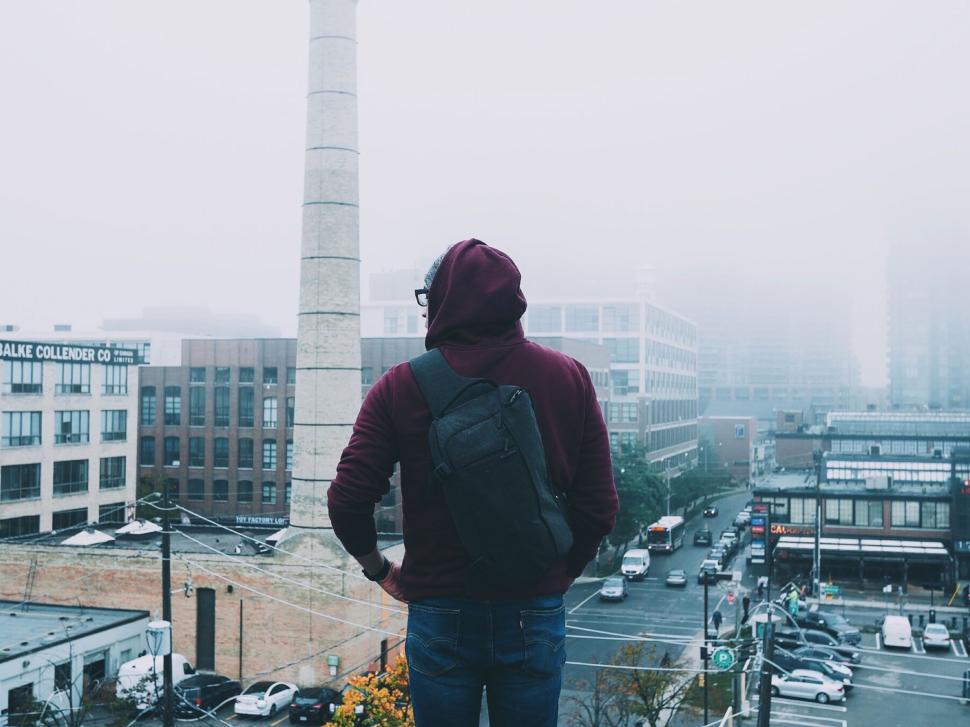 Free Image of Person in hoodie on a foggy rooftop overlooking urban scene. 