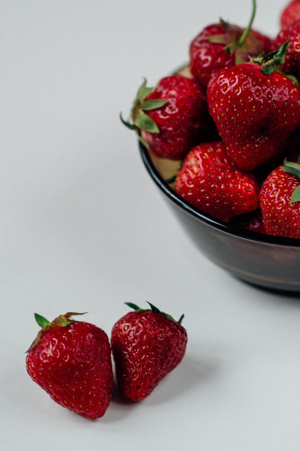Free Image of Fresh strawberries in a bowl with two strawberries beside. 