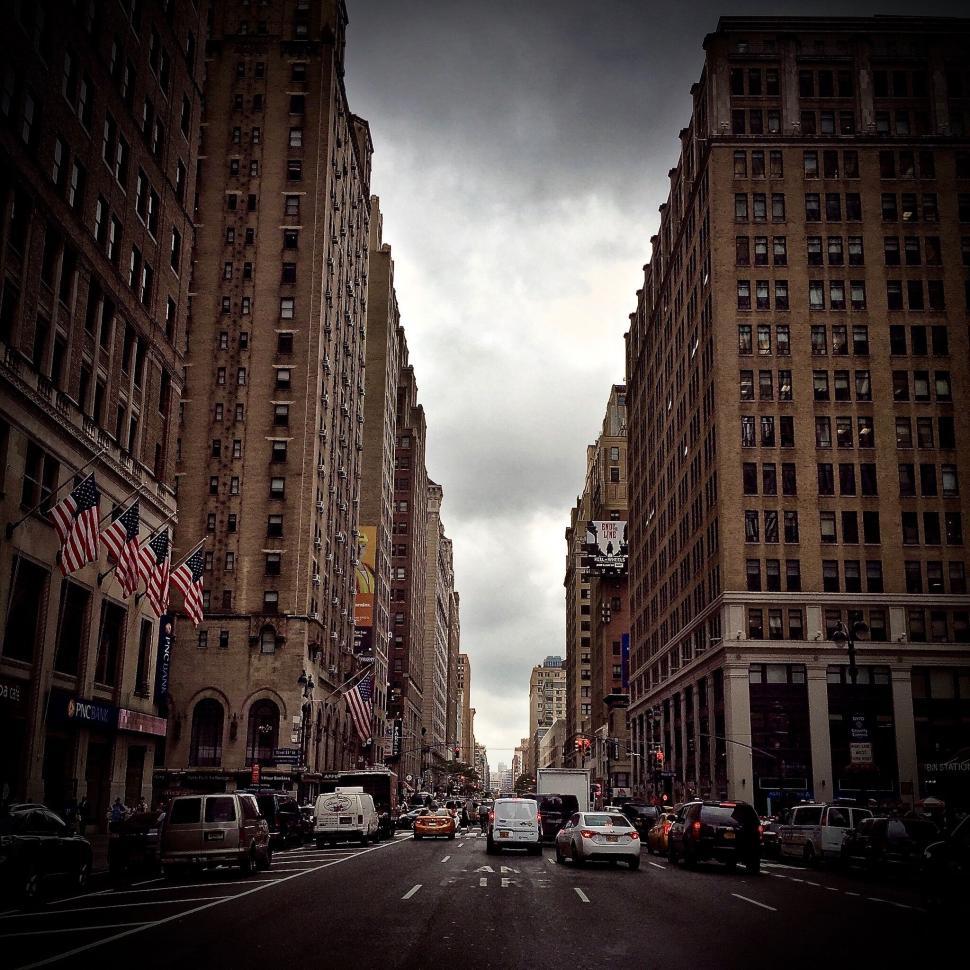 Free Image of Busy city street flanked by skyscrapers under cloudy sky 