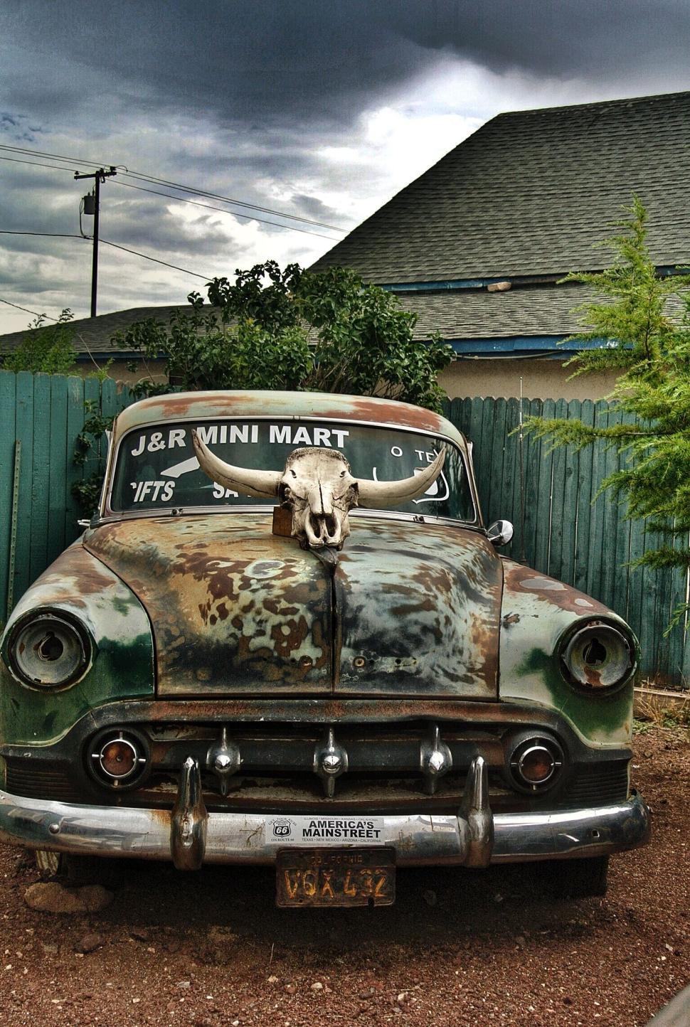 Free Image of Rusty old car adorned with skull in front of mini mart 