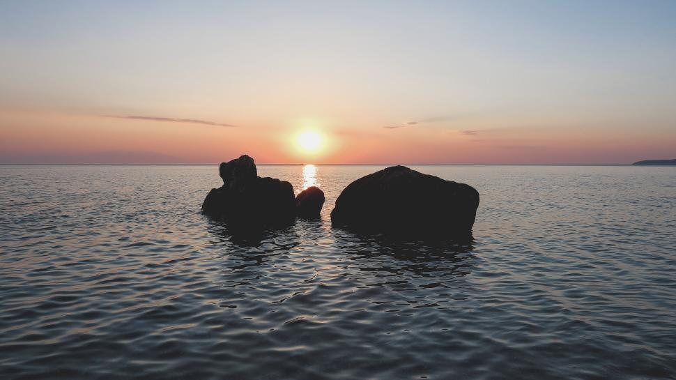 Free Image of Sunset over calm sea with large rocks in foreground 