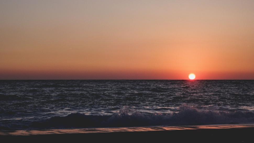 Free Image of Sunset over the ocean with gentle waves on the shore. 