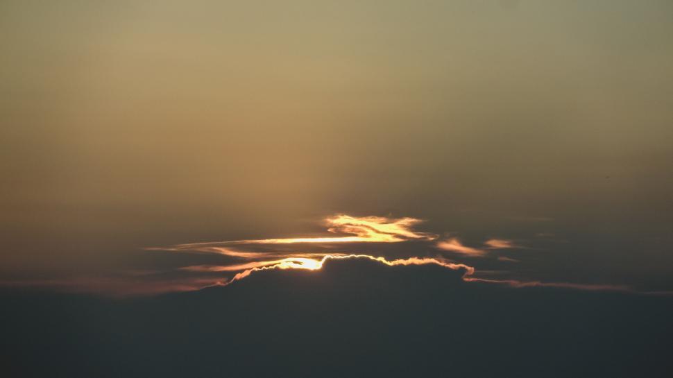 Free Image of Serene sunset behind clouds, warm golden hues glow. 