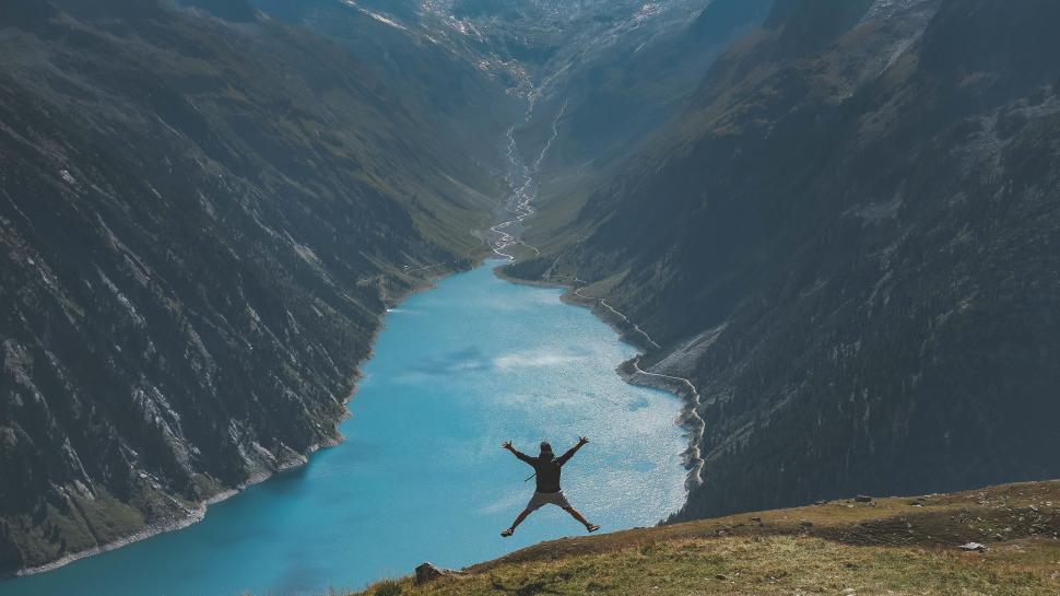 Free Image of Hiker jumping in joy above a scenic mountain lake view 