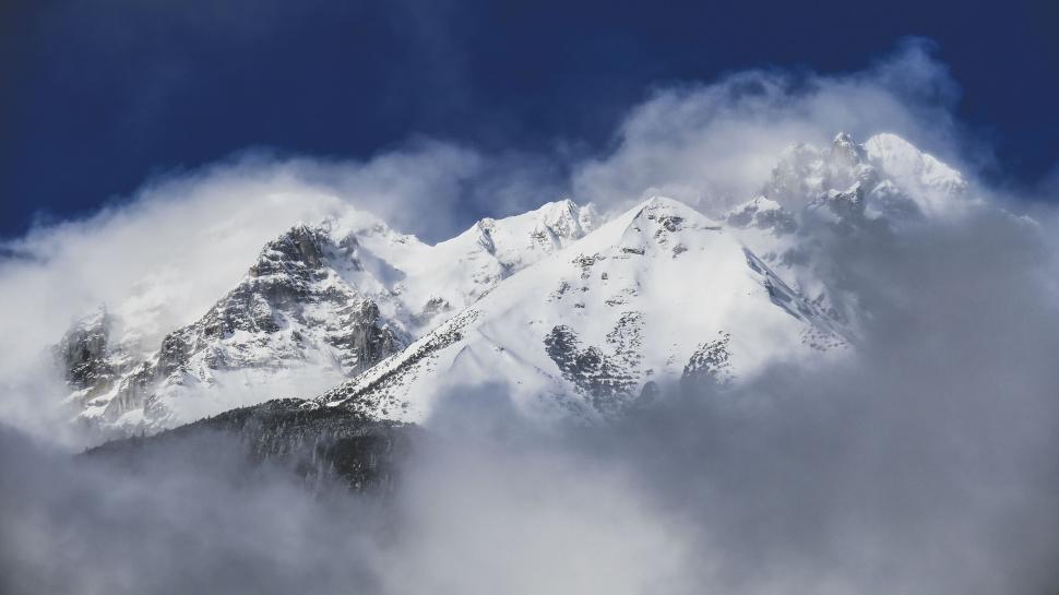 Free Image of Snow-capped mountains peeking through clouds in daylight 