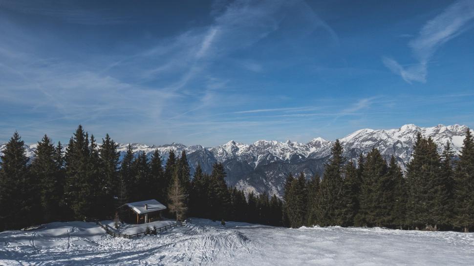 Free Image of Small cabin amidst snowy forest with mountains backdrop 