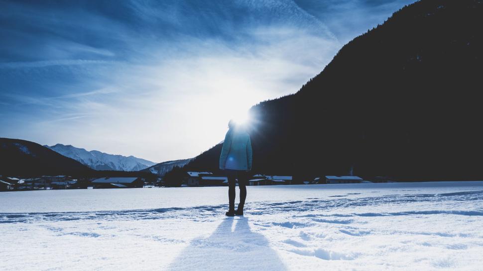 Free Image of Person standing on snowy field with sun setting behind. 
