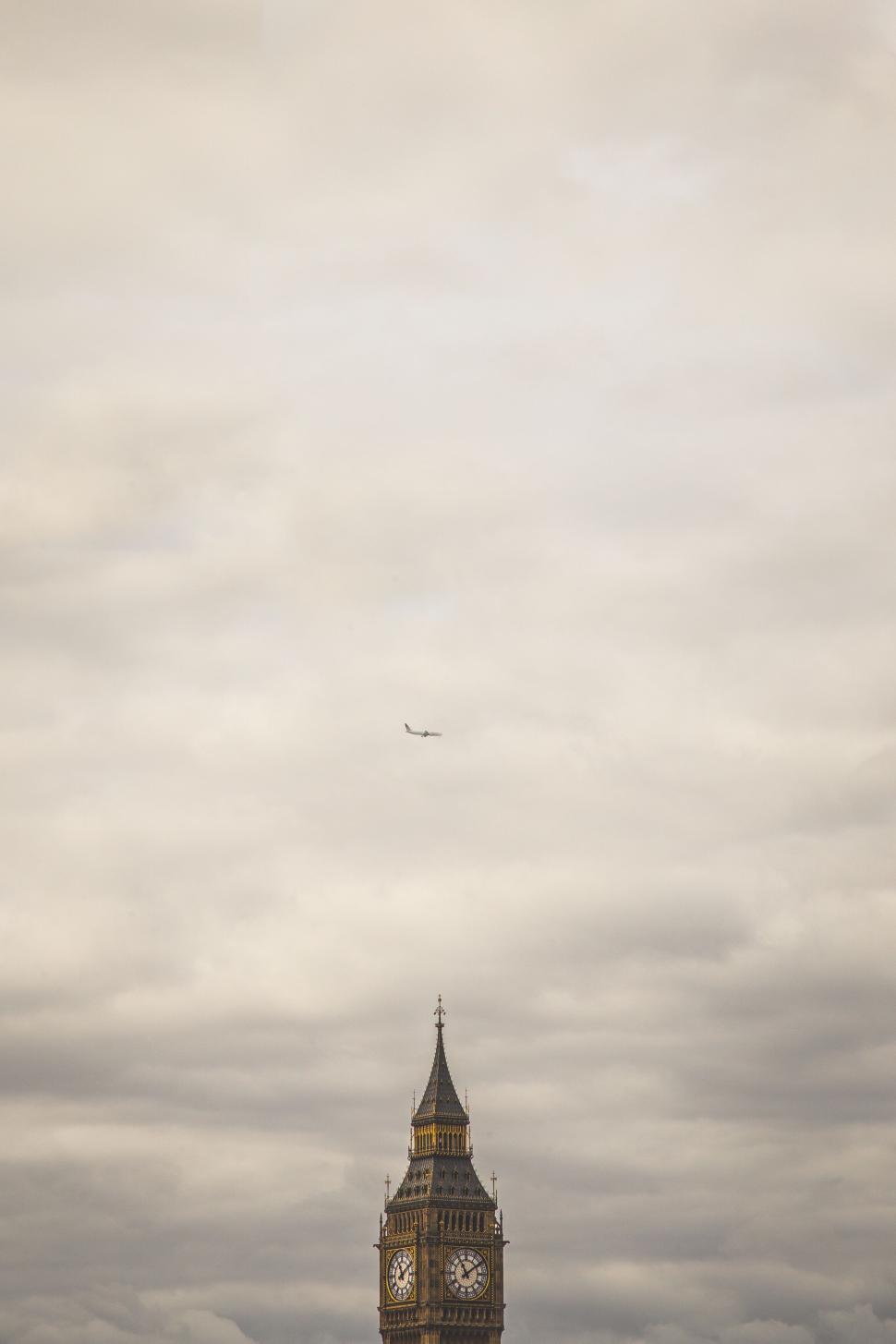 Free Image of View of Big Ben clock tower with airplane under cloudy sky 