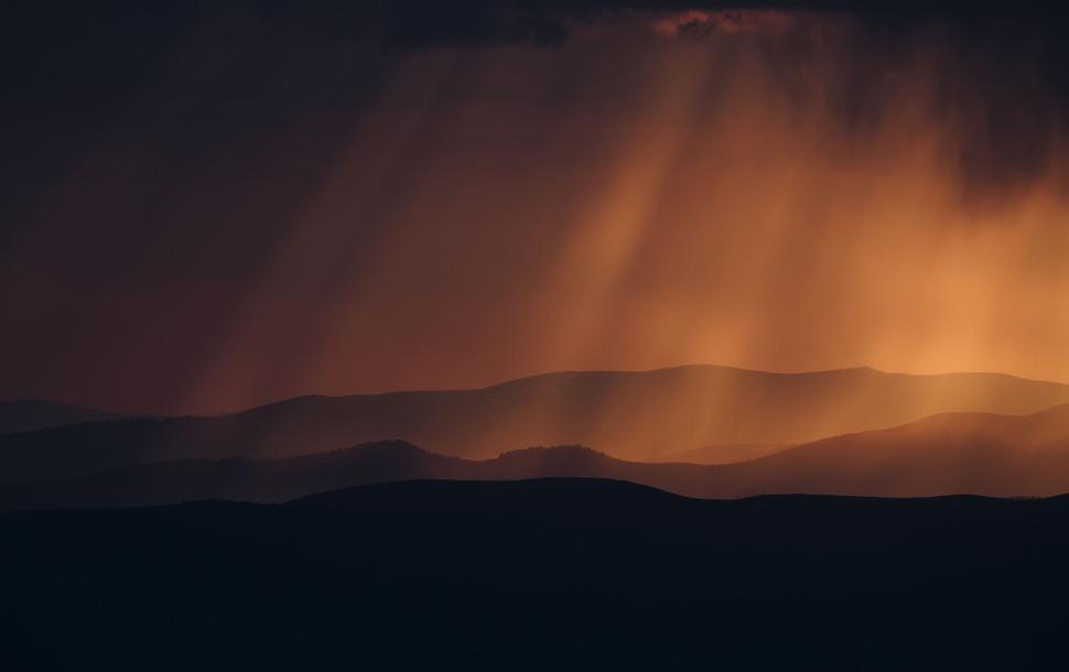 Free Image of Sun rays shine through clouds over mountain landscape 