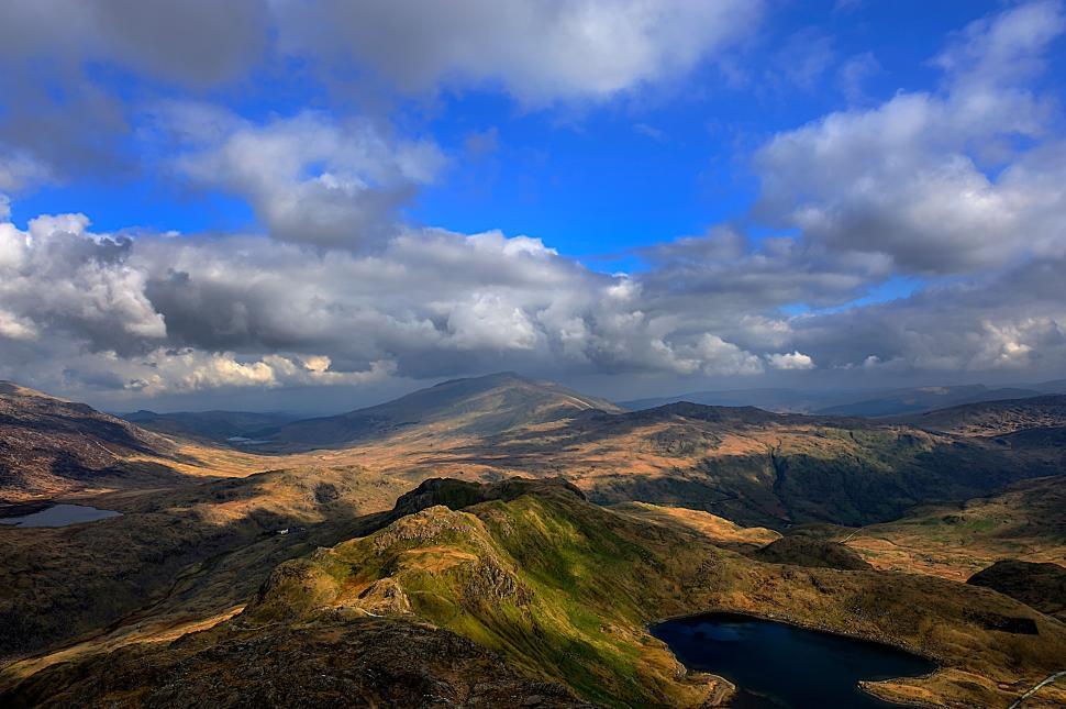 Free Image of Panoramic view of rolling hills under cloudy blue sky 