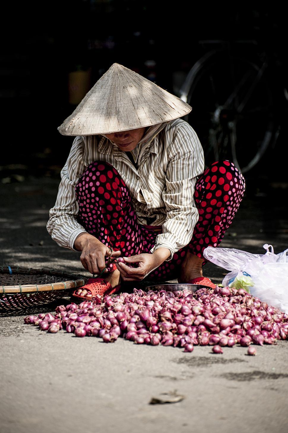 Free Image of Woman peeling shallots in traditional Asian market. 