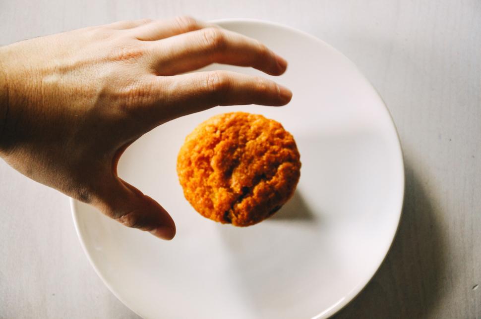 Free Image of Hand reaching for a muffin placed on a white plate. 