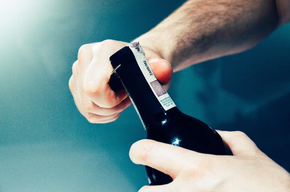 Free Image of Hand opening a bottle of wine using a corkscrew tool. 