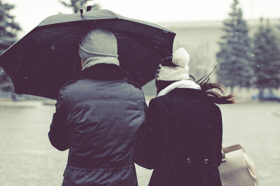 Free Image of Couple walking under umbrella in snowy urban setting 