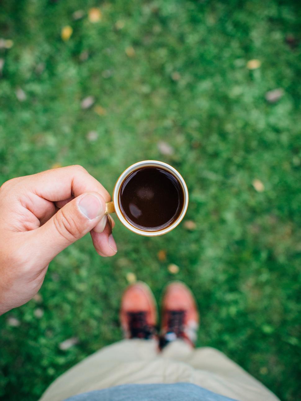 Free Image of Person holding cup of coffee over green grass view 
