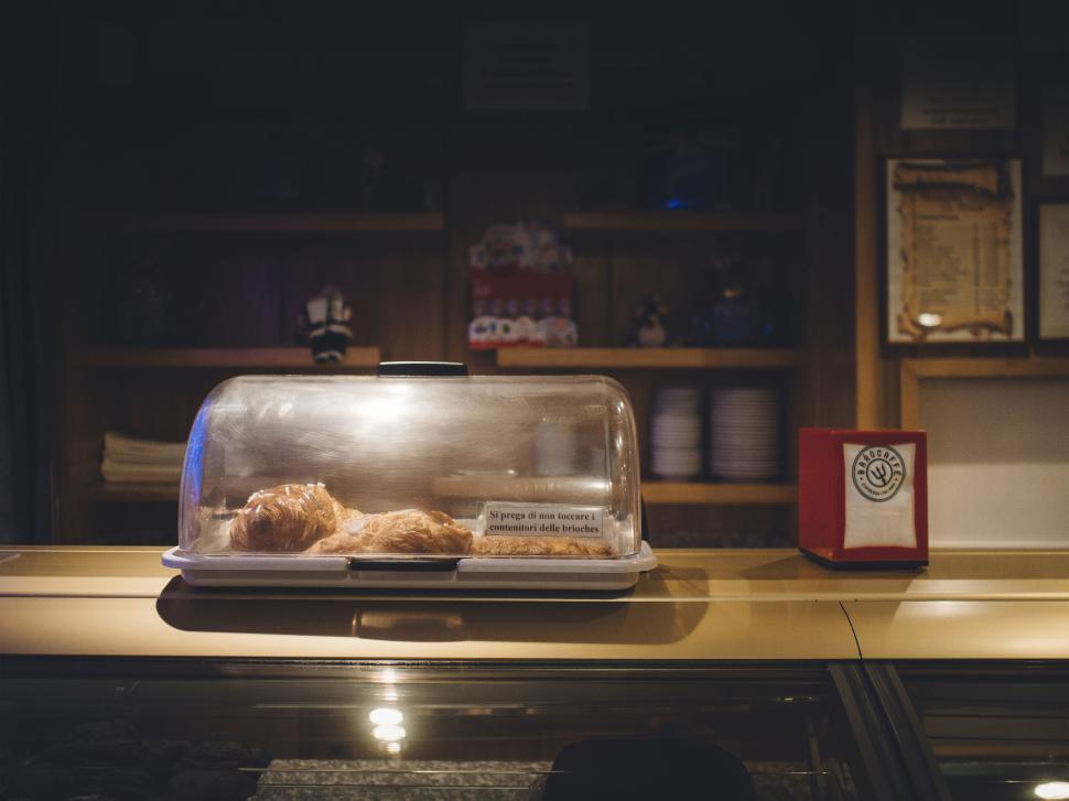 Free Image of Pastries under a glass cover on a cozy rustic counter. 