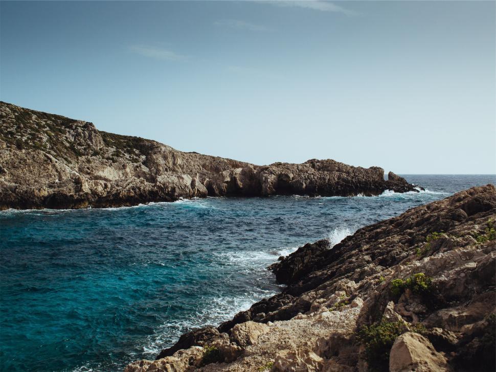 Free Image of Rocky coastline meeting clear blue waters under bright sky. 