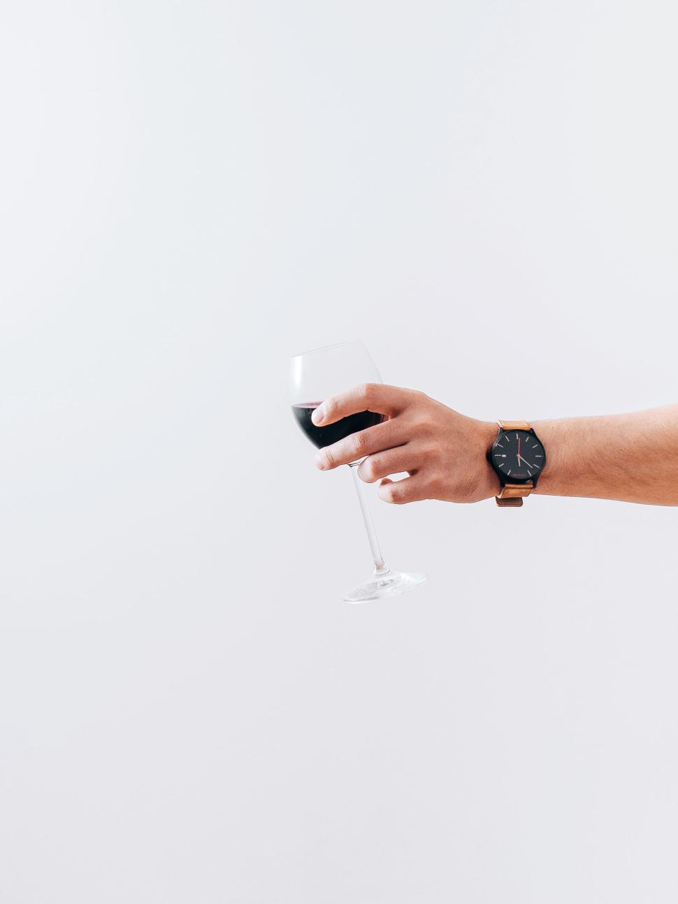 Free Image of Hand holding a glass of red wine against a white wall. 