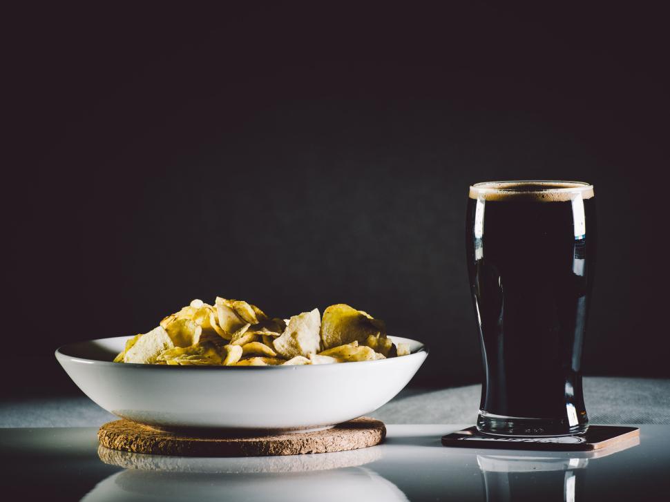 Free Image of Glass of dark beer paired with bowl of potato chips. 