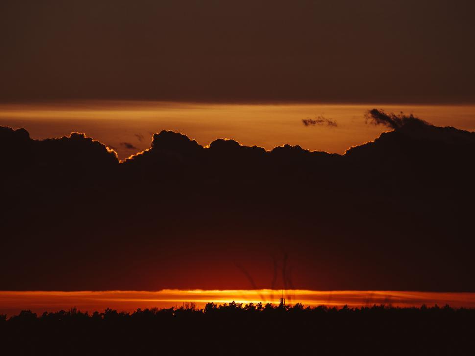 Free Image of Sunset with golden clouds above darkened landscape horizon. 