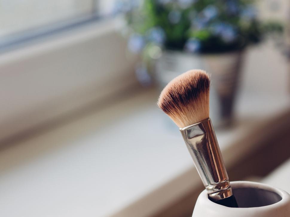 Free Image of Makeup brush in container by windowsill with flowers. 