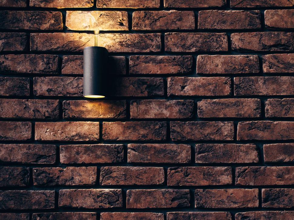 Free Image of Brick wall with light fixture casting a warm glow on it. 