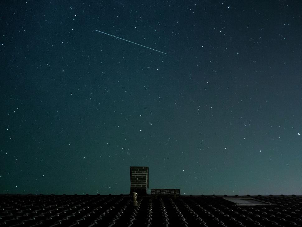 Free Image of Starry night sky with a shooting star above a rooftop. 